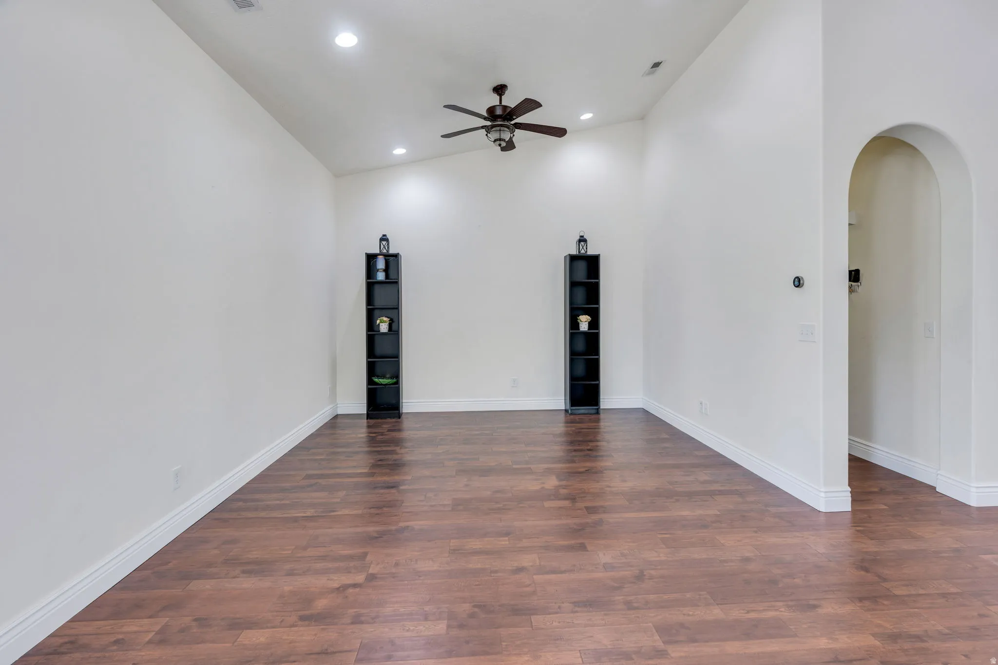 Vaulted ceiling with recessed lighting, wood-finish flooring, ceiling fan, and arched doorway
