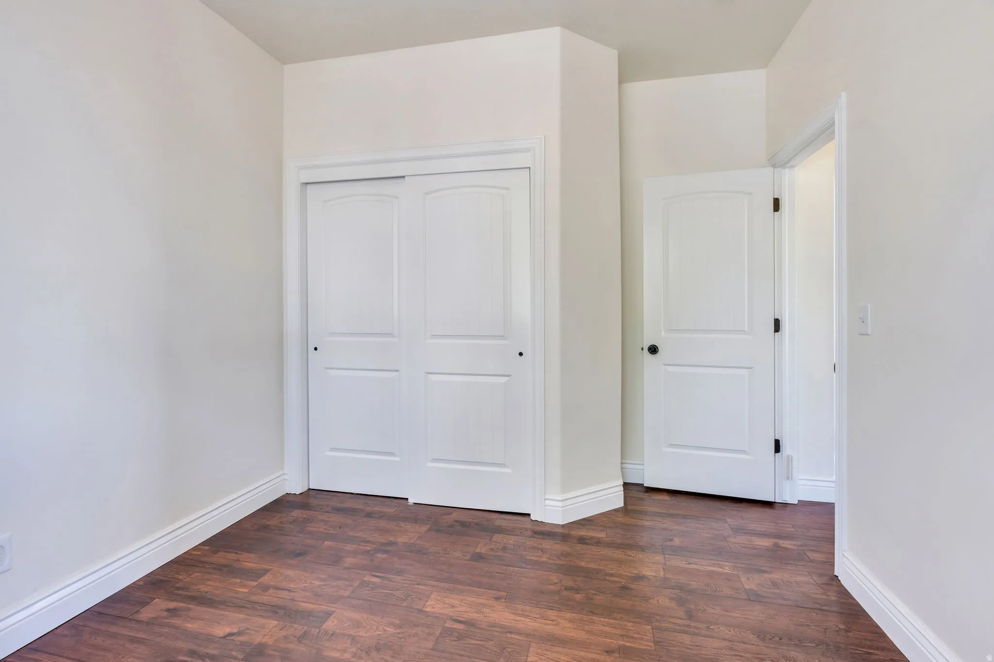 Wood-finish flooring with white baseboards, a white paneled door, and a white sliding closet door