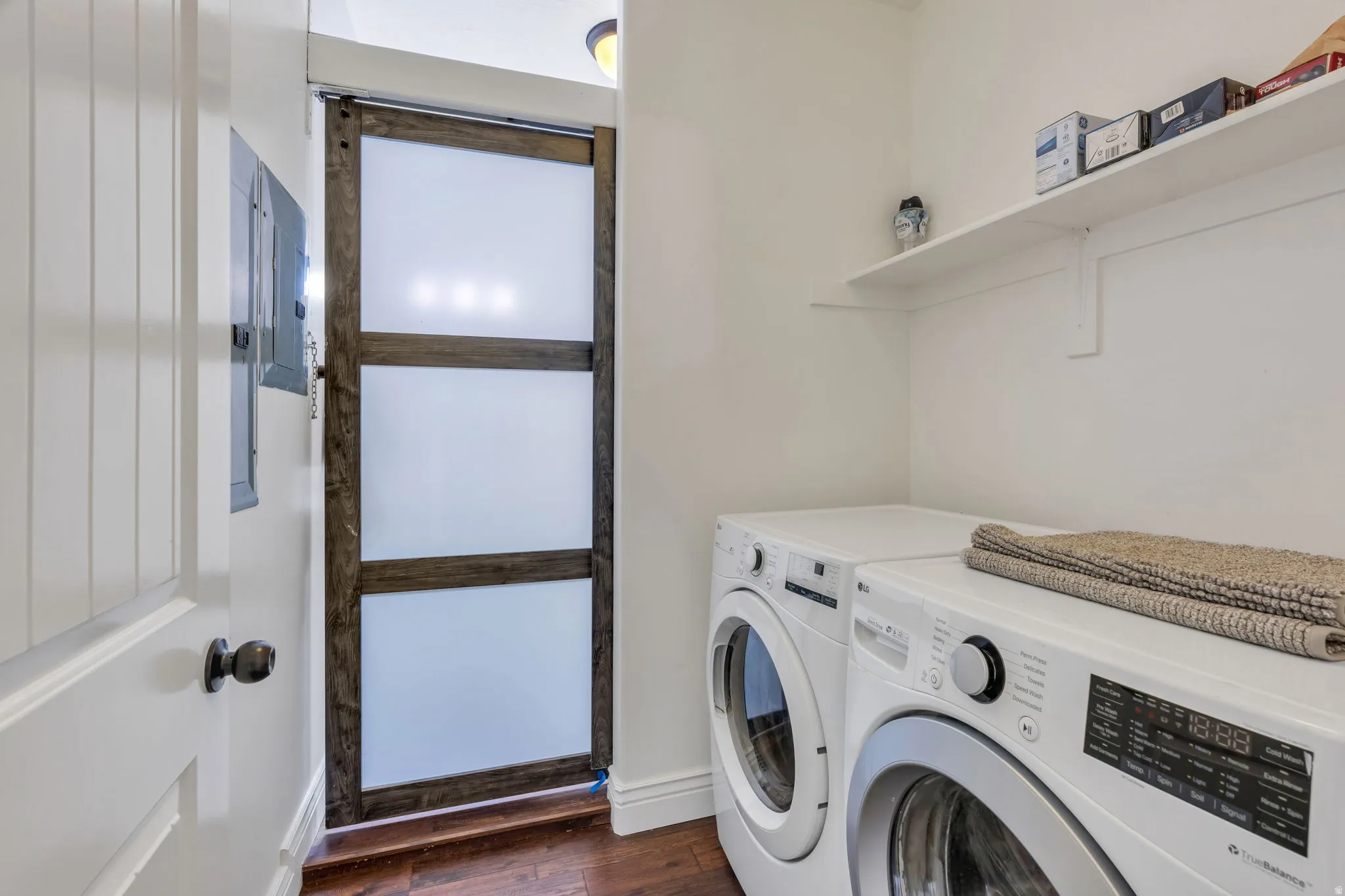 Dedicated laundry area featuring a wall-mounted shelf, rich wood-finish flooring, and a modern sliding door with frosted panels