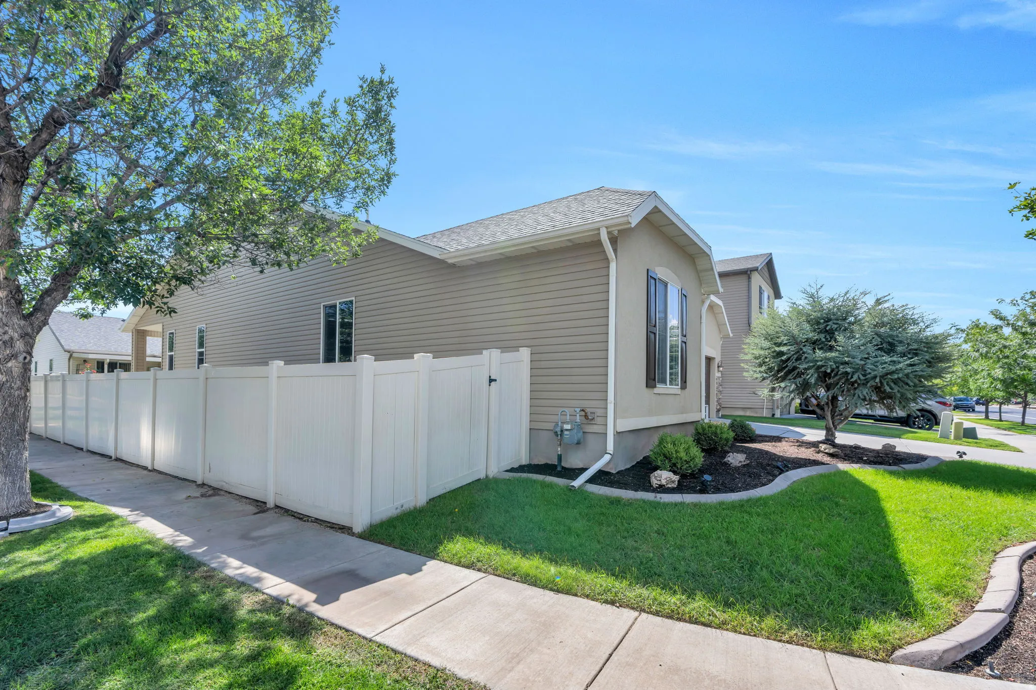 Exterior siding, white fencing, concrete sidewalk, established tree, and landscaped garden beds