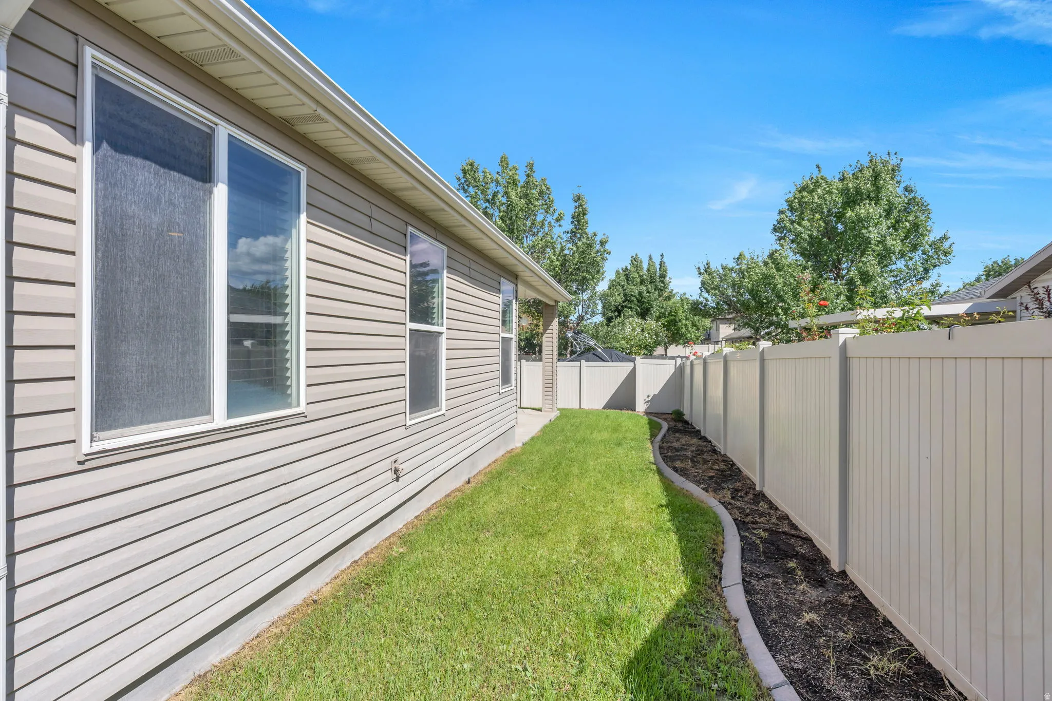 Siding exterior with multiple windows, a manicured lawn, and a light-colored privacy fence