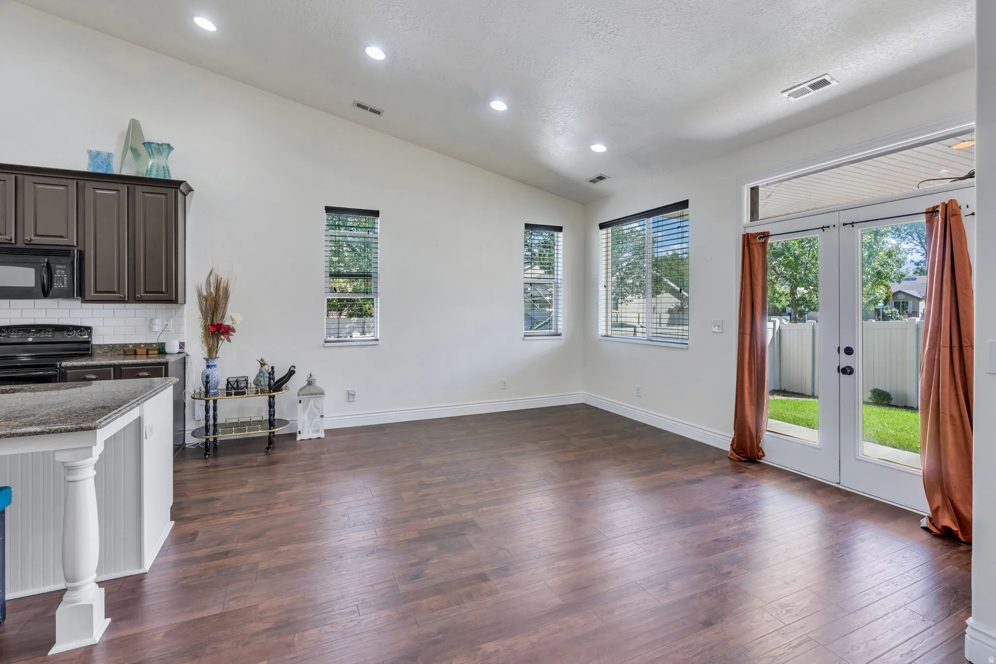 Vaulted ceilings, recessed lighting, wood-finish flooring, French doors, and a kitchen island with a stone-finish countertop