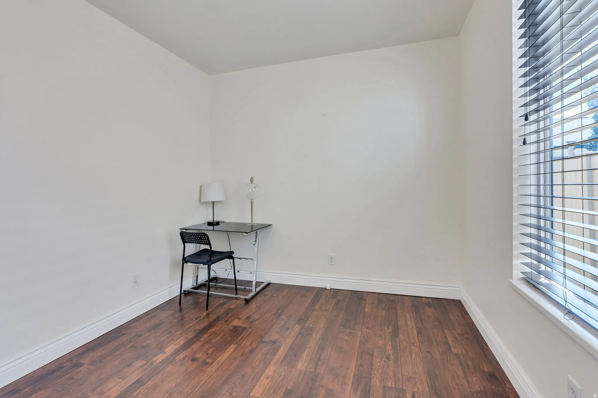 Wood-finish flooring with white baseboards, a white wall finish, and a window with horizontal blinds