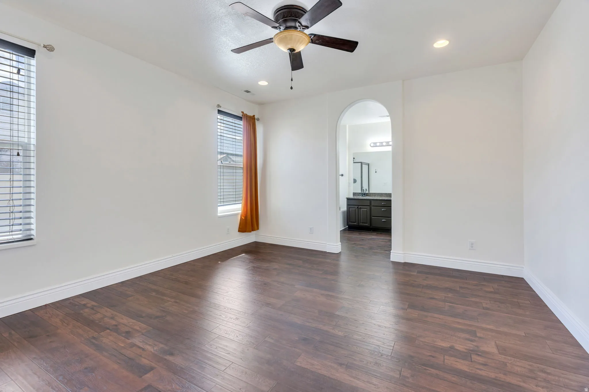 Spacious primary room featuring wood-finish flooring, two windows with blinds, a ceiling fan, and recessed lighting