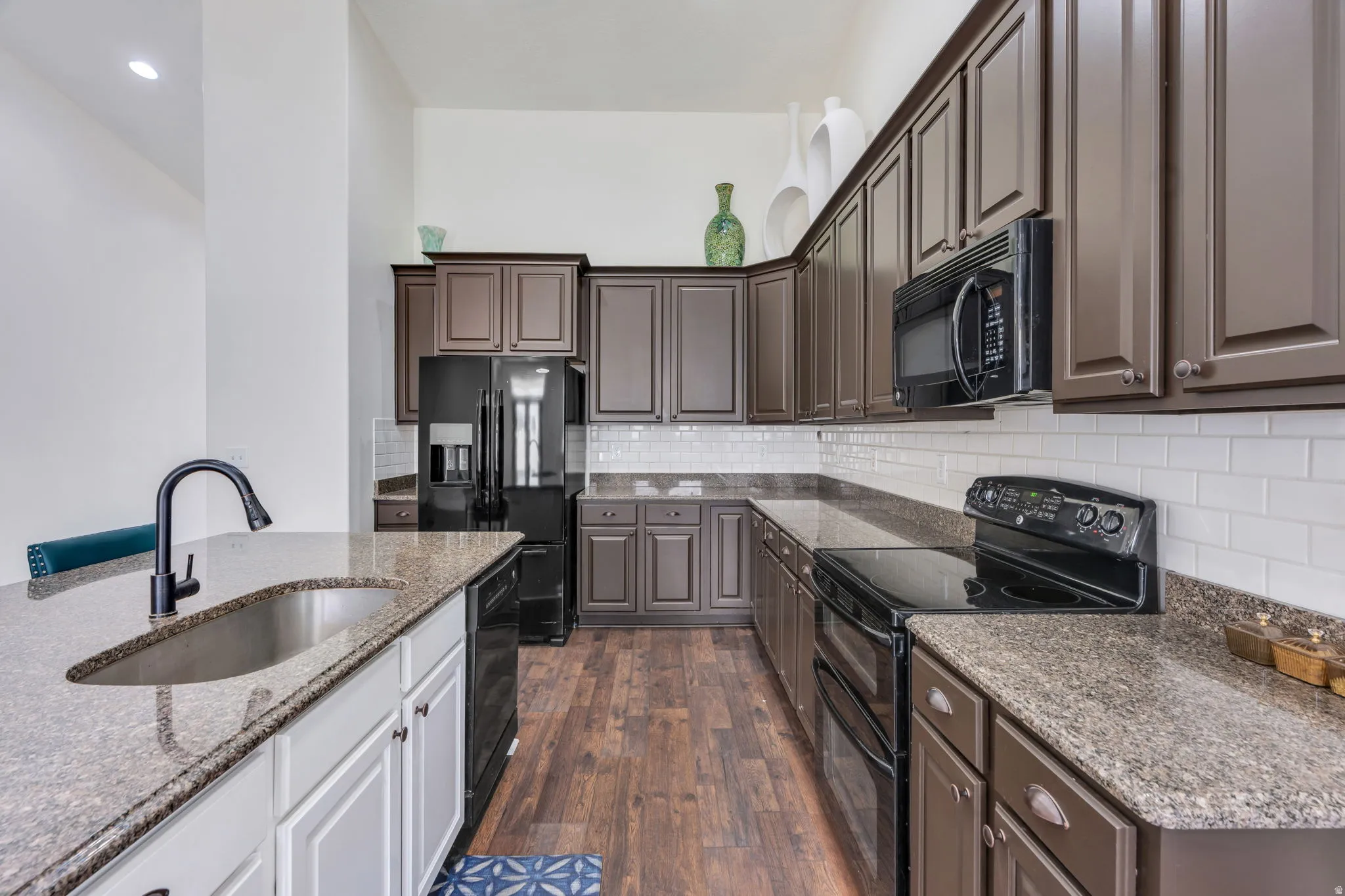 Kitchen featuring wood-finish flooring, white subway tile backsplash, dark-toned cabinetry, and integrated appliances