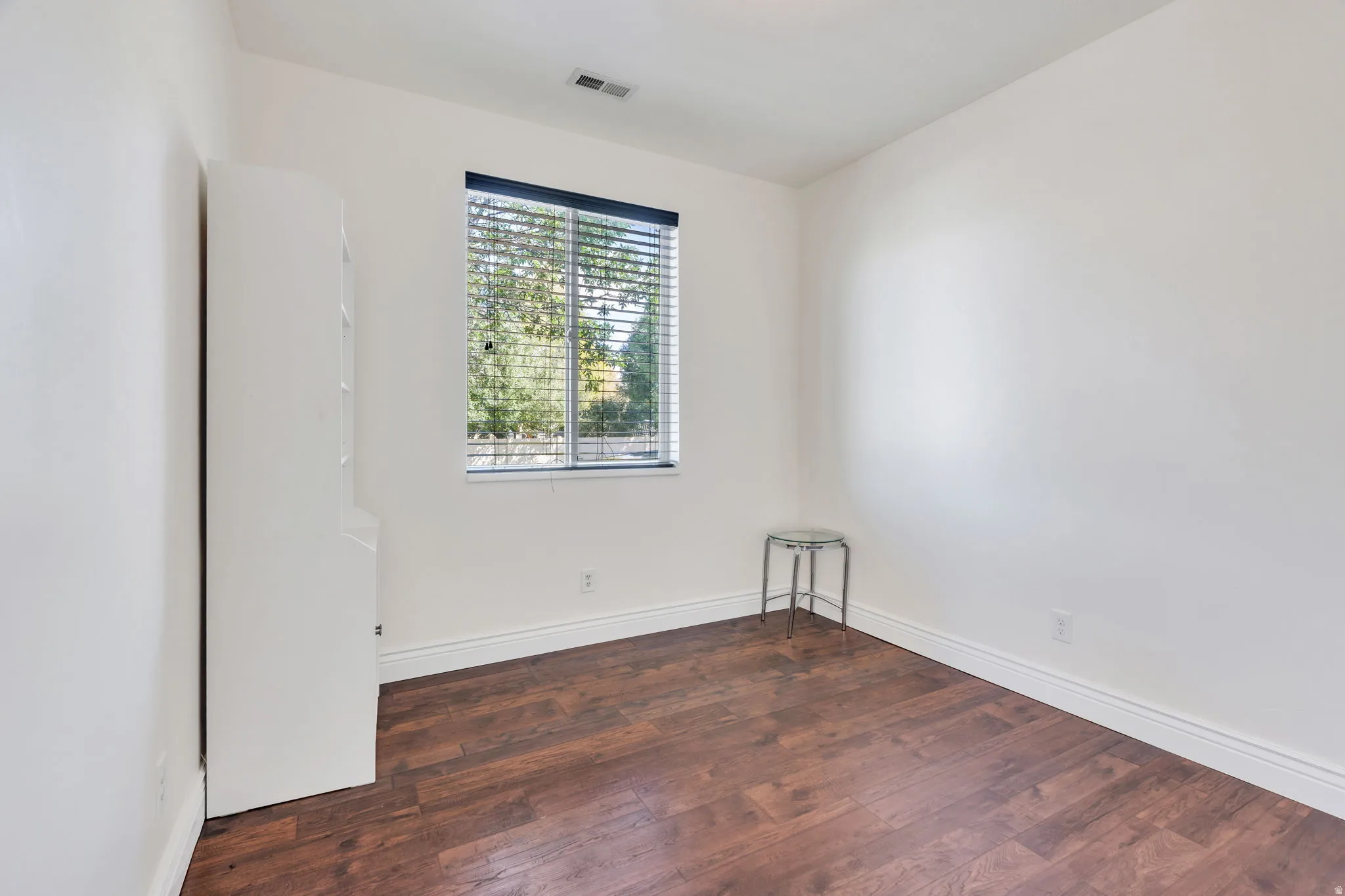 Wood-finish flooring with white trim and a window with horizontal blinds