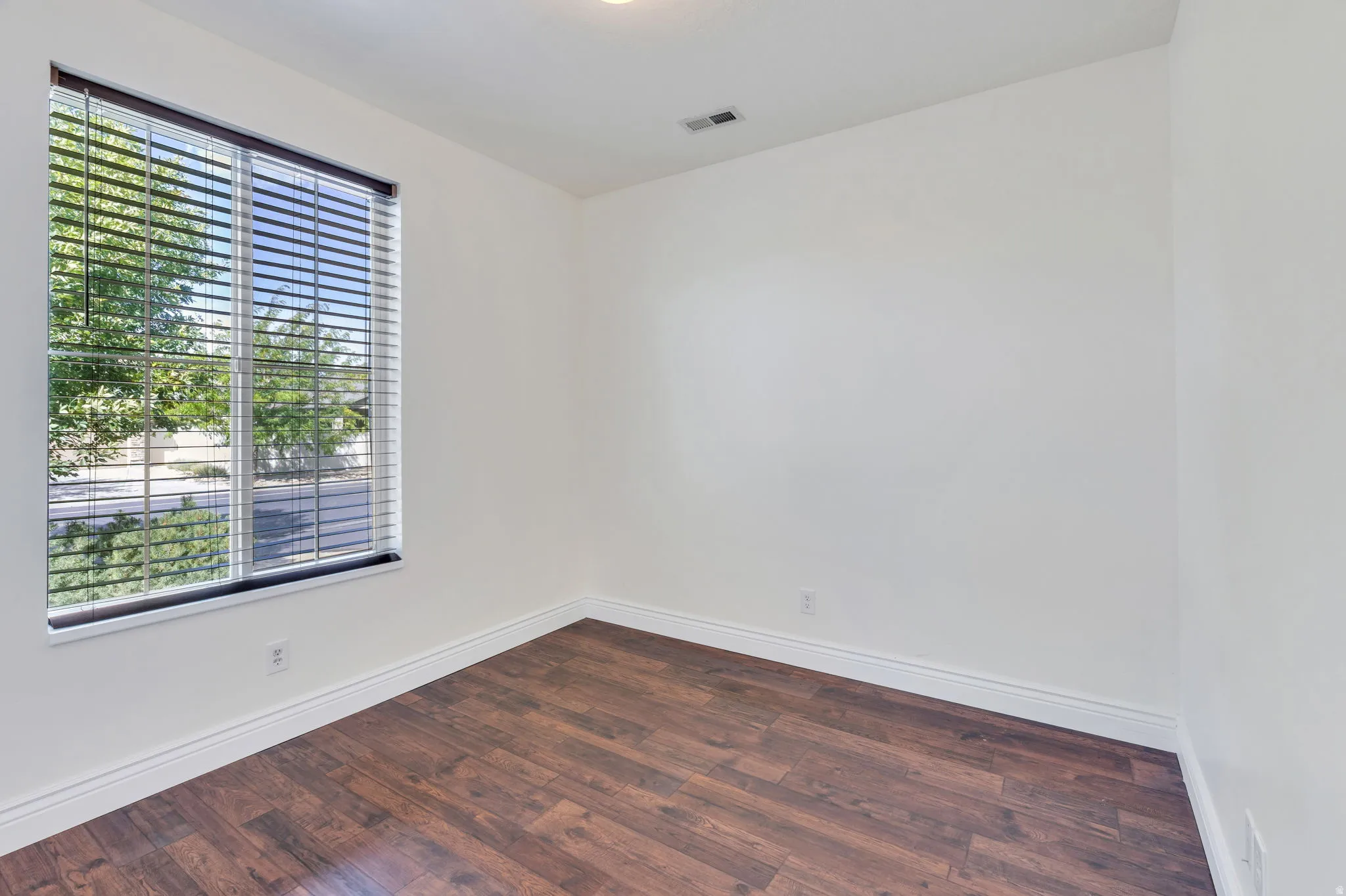 Wood-finish flooring, white walls, and a window with blinds