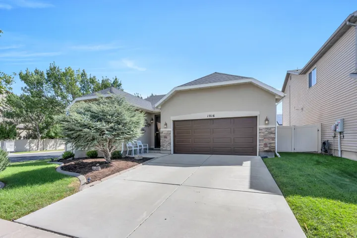 Stucco exterior with stone accents, concrete driveway, attached two-car garage, and a covered entryway