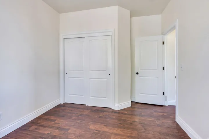 Wood-finish flooring with white baseboards, a white paneled door, and a white sliding closet door