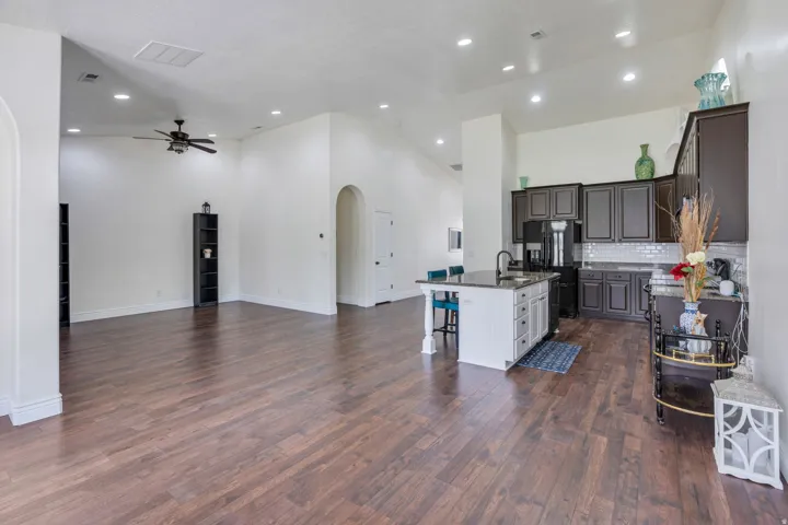 Expansive wood-finish flooring throughout, vaulted ceilings, recessed lighting, kitchen island with seating, and dark wood-finish cabinetry