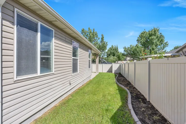 Siding exterior with multiple windows, a manicured lawn, and a light-colored privacy fence