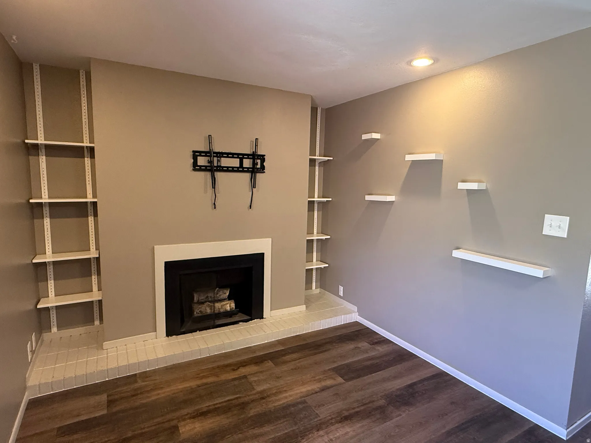 Fireplace with white surround and hearth, built-in shelving, recessed lighting, and wood-finish flooring