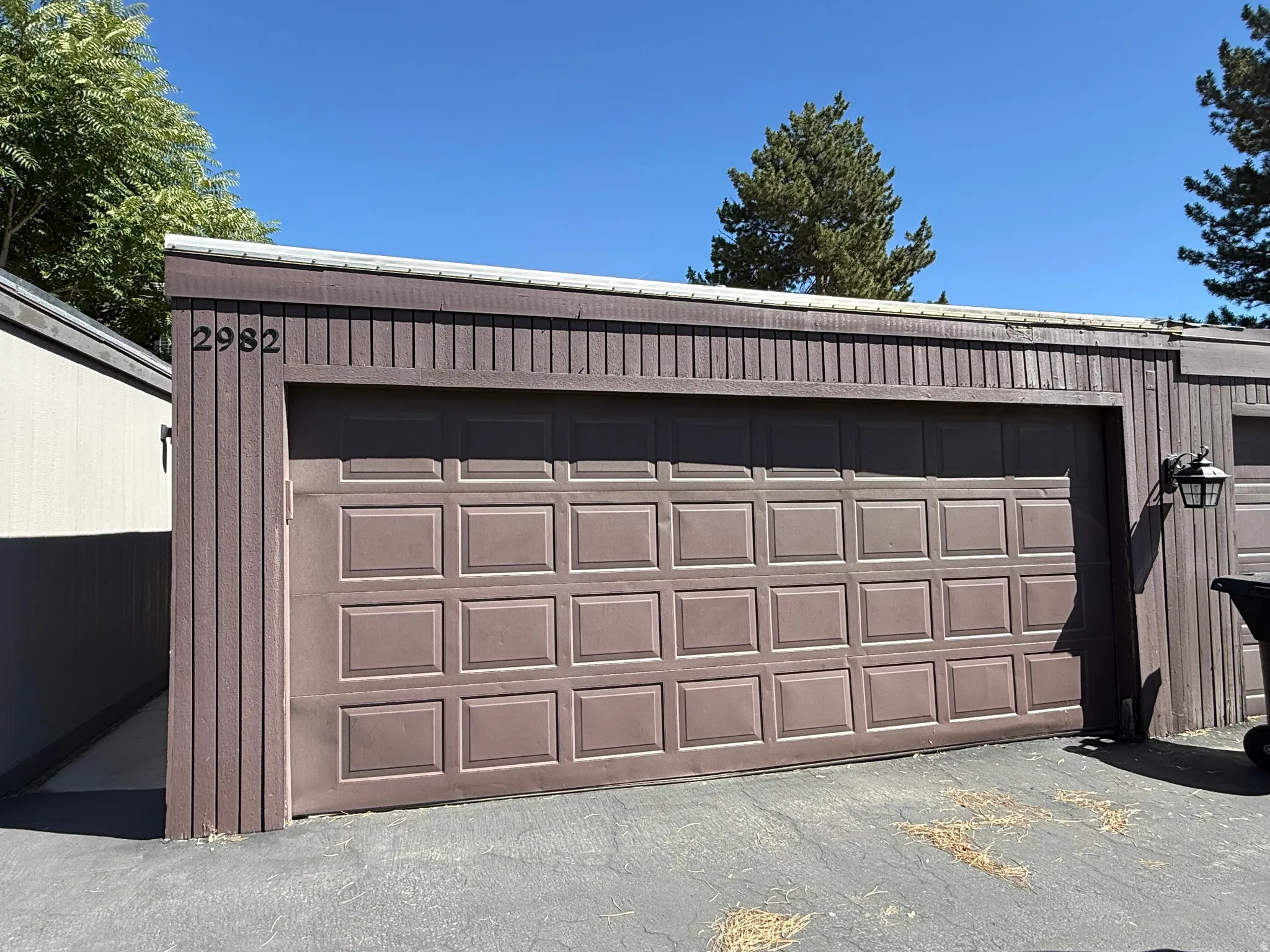 Brown paneled garage door with vertical wood siding and exterior wall lantern