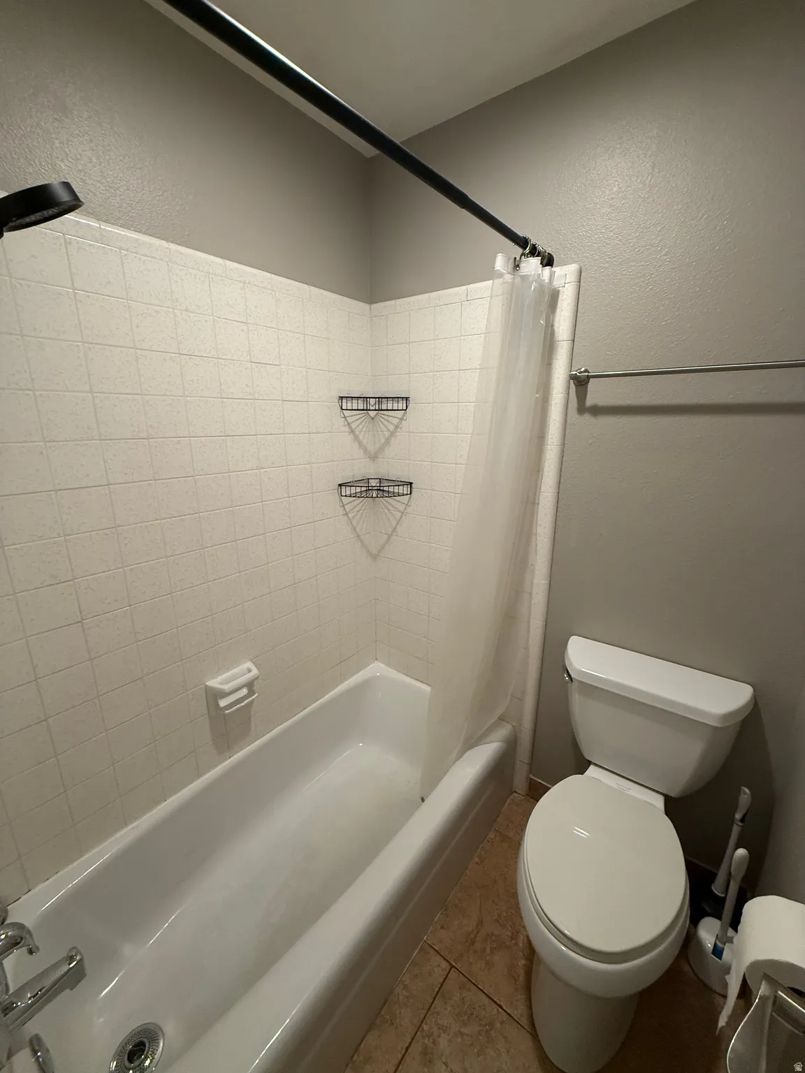 Bathtub with white tile surround, floor-mounted toilet, and tan floor tiling
