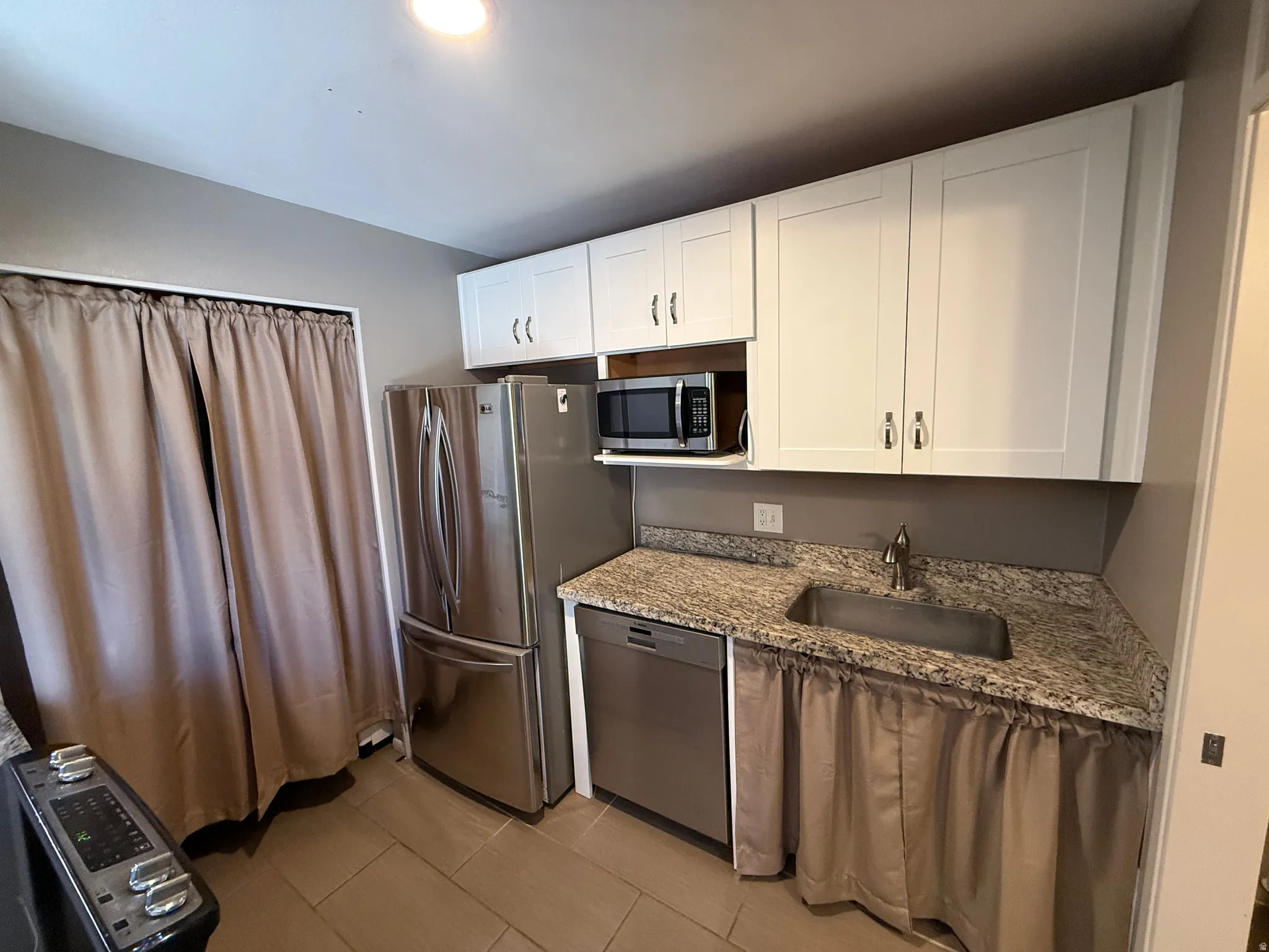 White shaker-style cabinetry, granite-style countertops, stainless steel sink, stainless steel dishwasher, and stainless steel refrigerator