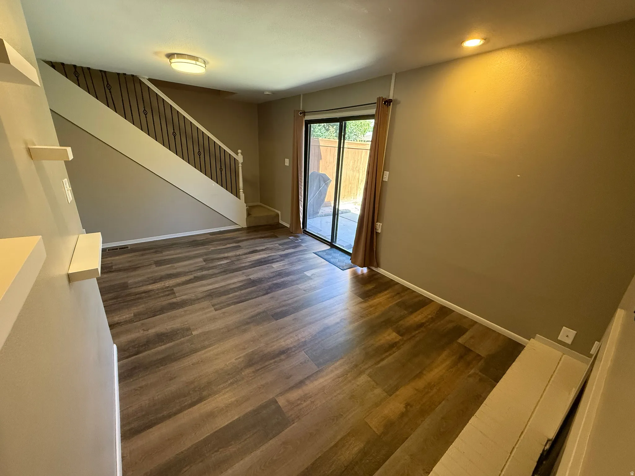 Wood-finish flooring, staircase with wrought iron balusters, recessed lighting, built-in shelving, and sliding glass door