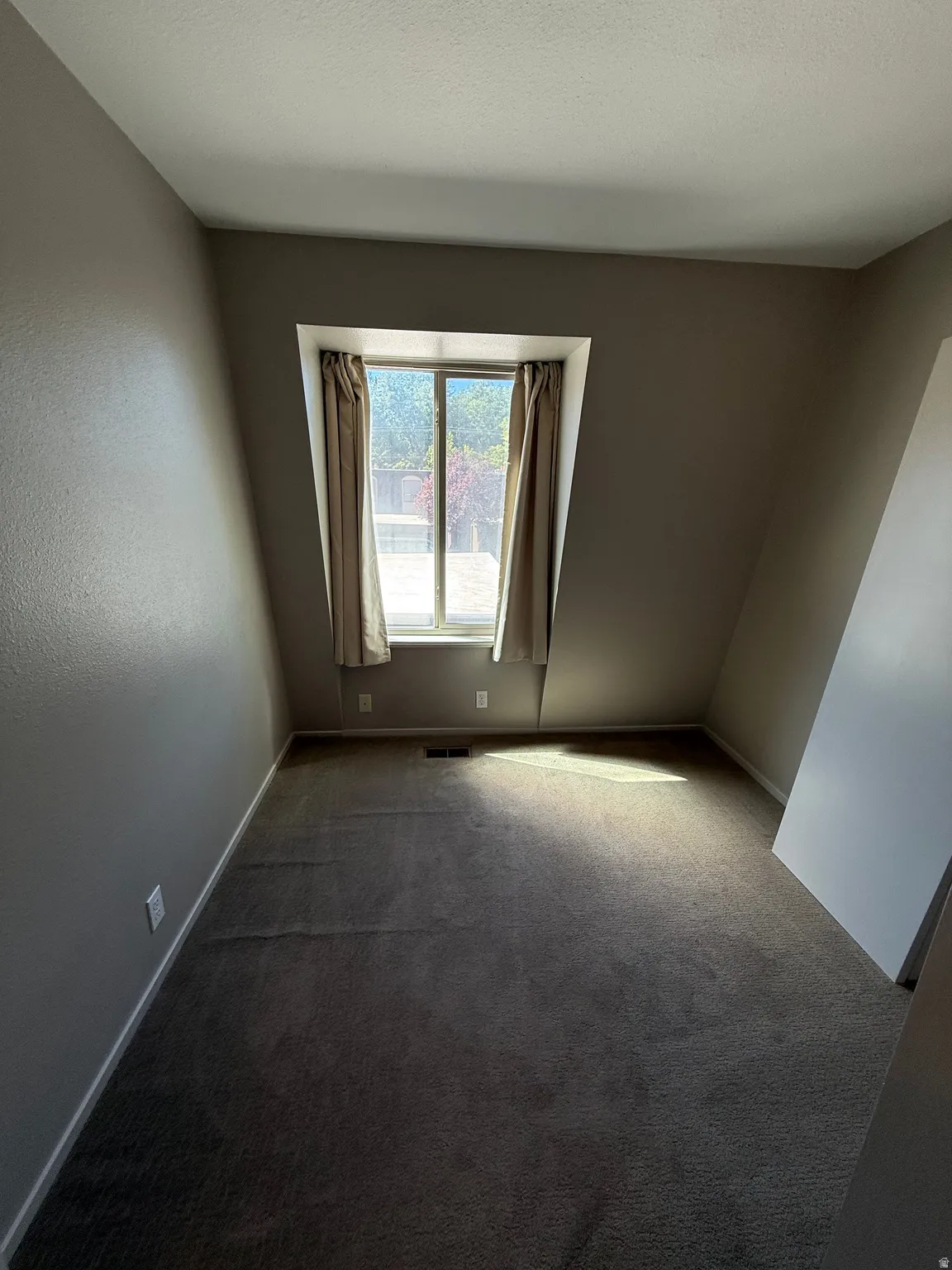 Carpeted flooring, sloped ceiling, window with curtain rods and curtains
