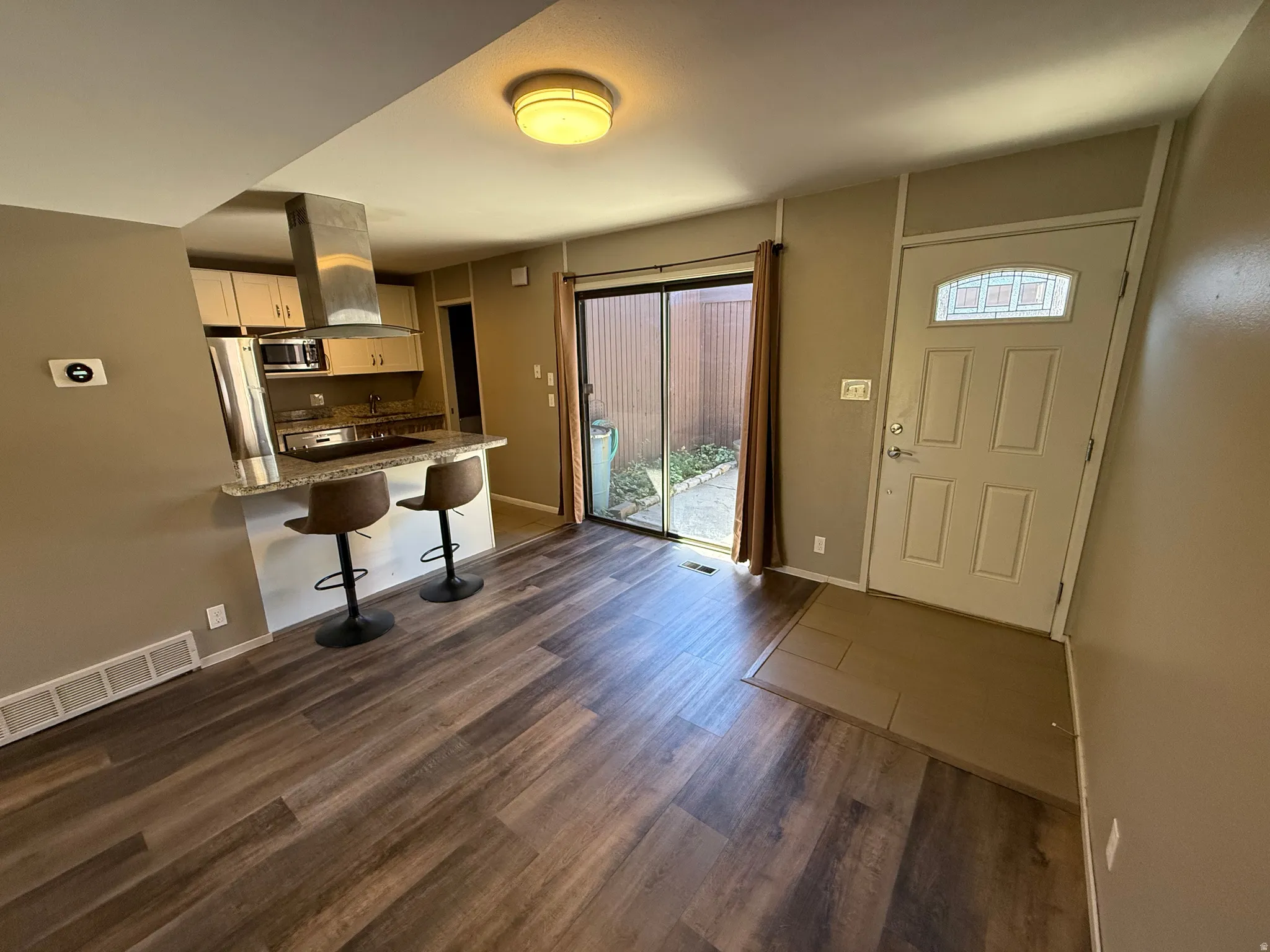 Wood-finish flooring throughout, kitchen with stone countertops, stainless steel appliances, and a breakfast bar