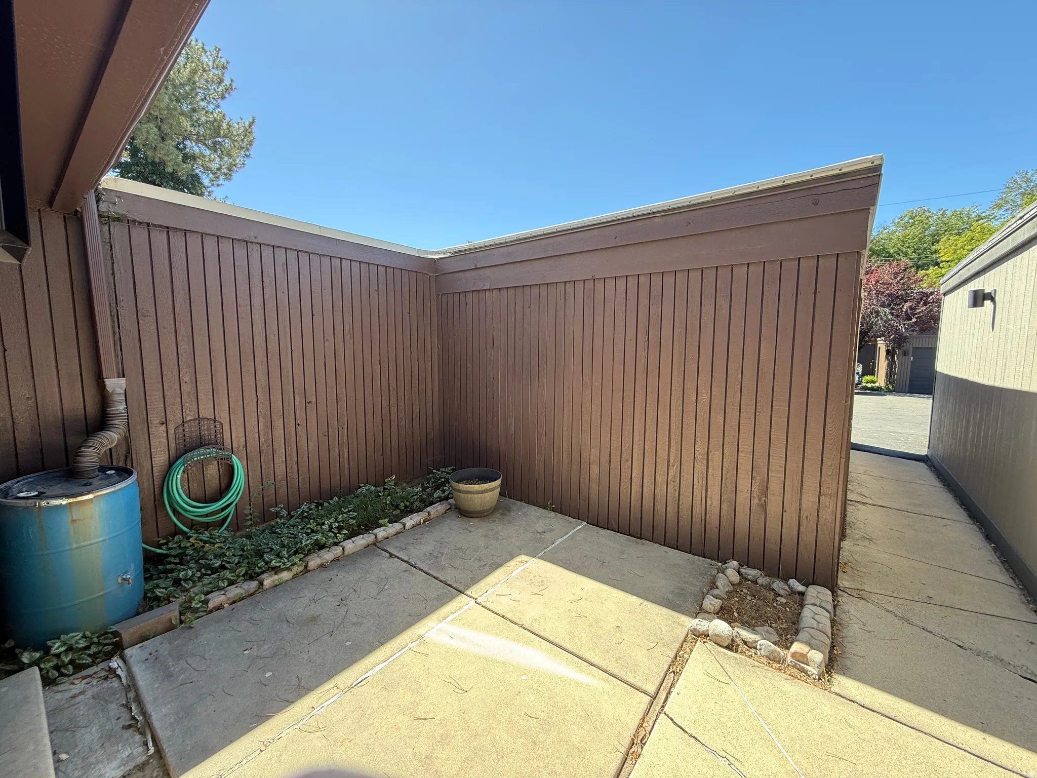 Concrete patio area with a privacy fence, defined planting beds, and a perimeter wall-mounted light fixture