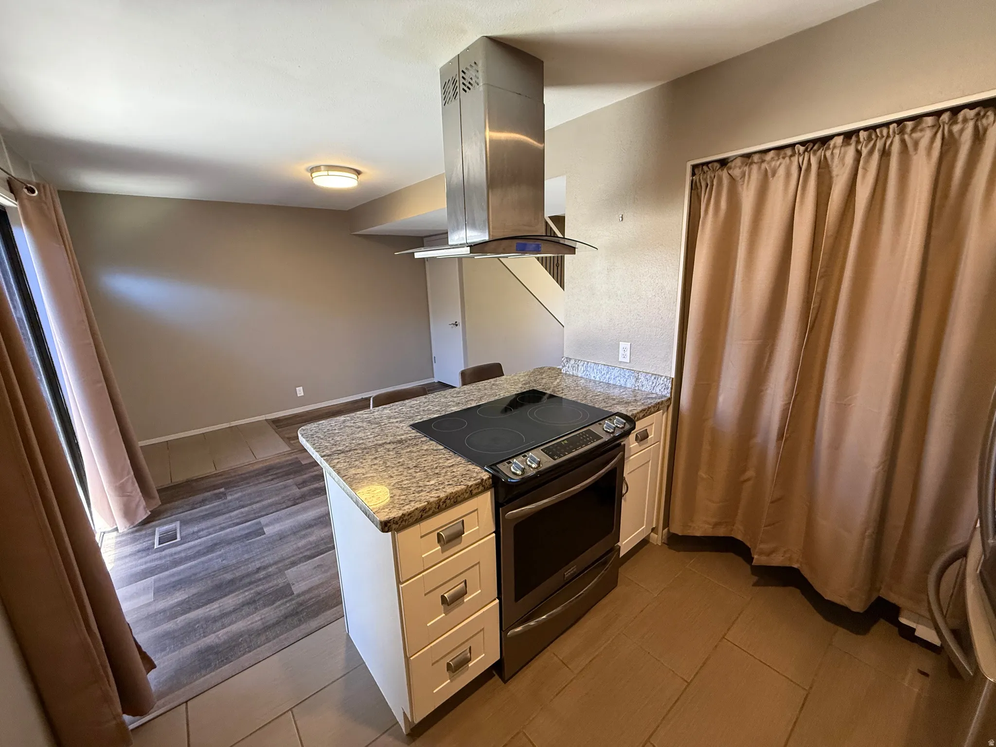 Kitchen island featuring a built-in electric range, stainless steel vent hood, and granite countertops