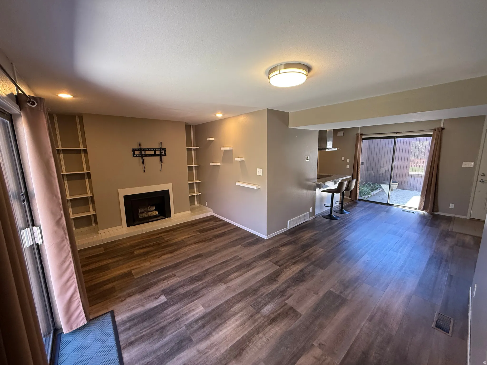 Wood-finish flooring throughout, fireplace with a white tile hearth, built-in shelving, and a sliding glass door to an outdoor patio space