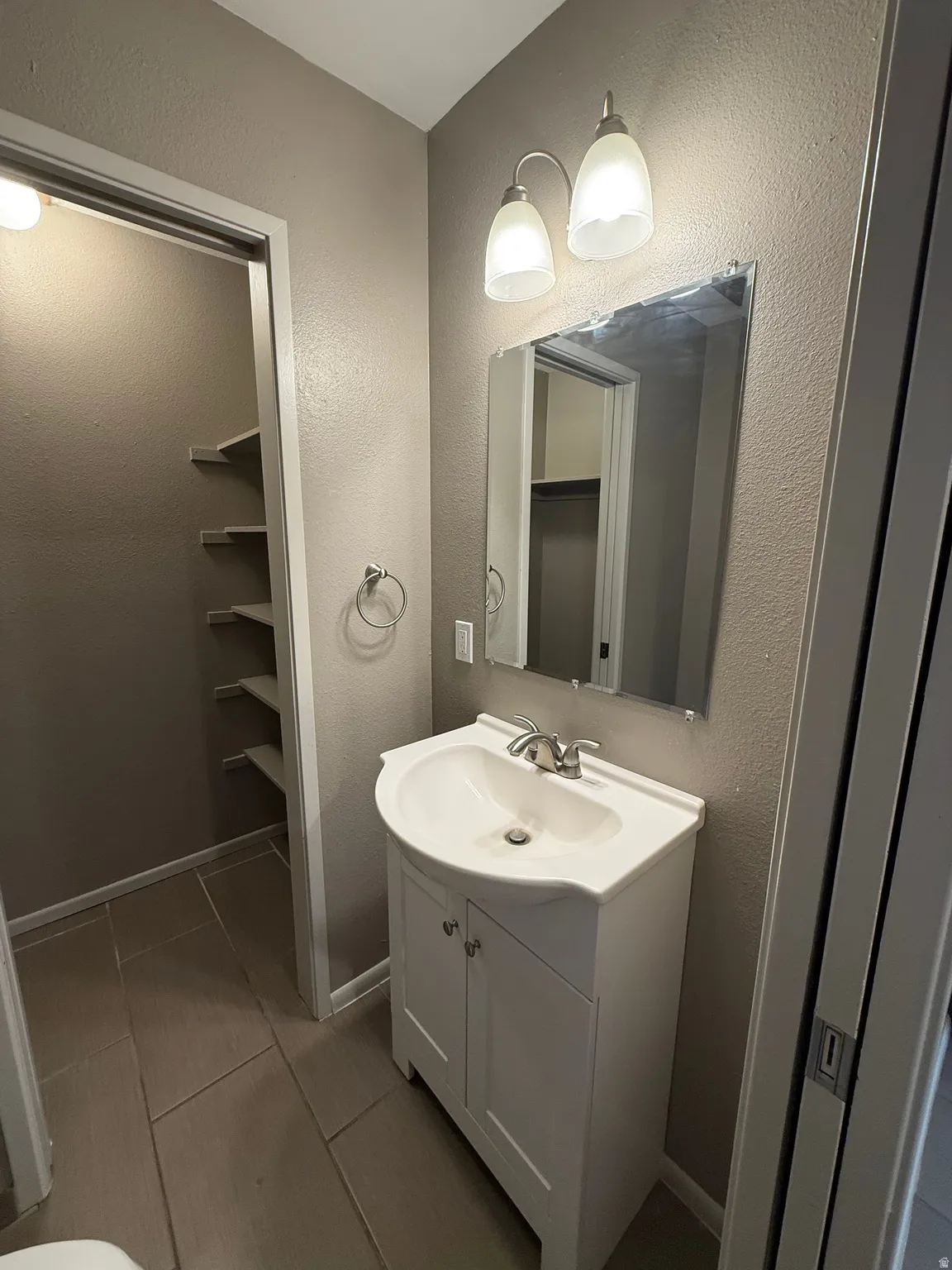 Bathroom featuring a white vanity with integrated sink, brushed nickel faucet, wall-mounted mirror, and decorative light fixture