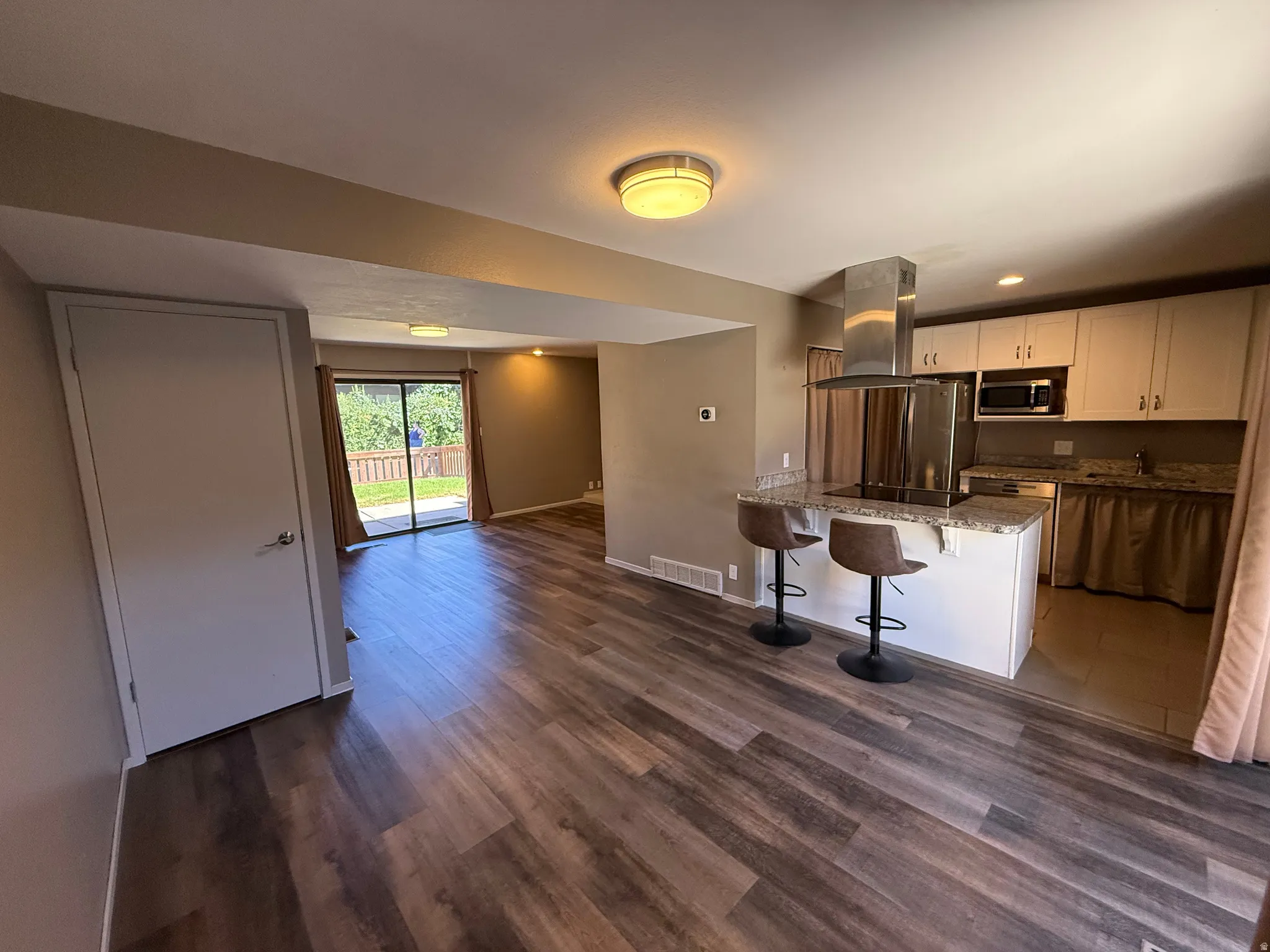 Wood-finish flooring throughout, kitchen island with seating, stainless steel range hood, white cabinetry, and sliding glass door access to the outdoor area