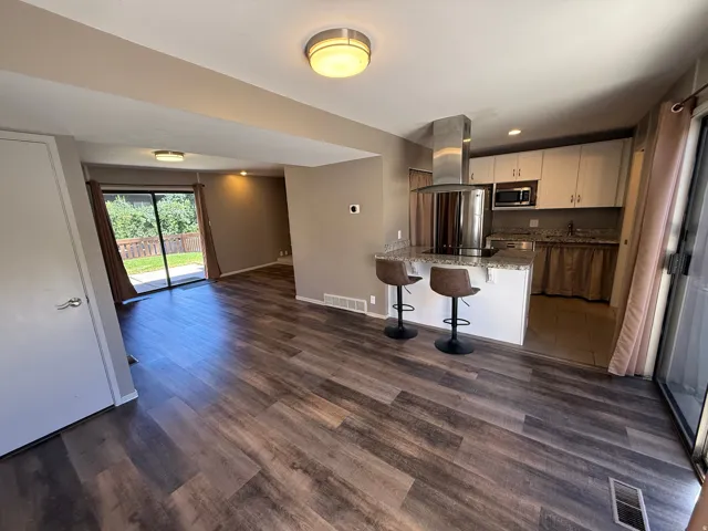 Wood-finish flooring throughout, kitchen island with built-in cooktop, stainless steel range hood, light-toned cabinetry, and sliding glass door access to outdoor space