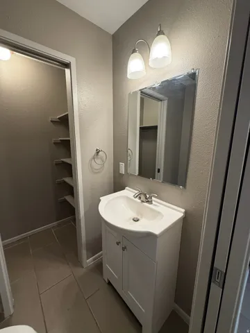 Bathroom featuring a white vanity with integrated sink, brushed nickel faucet, wall-mounted mirror, and decorative light fixture
