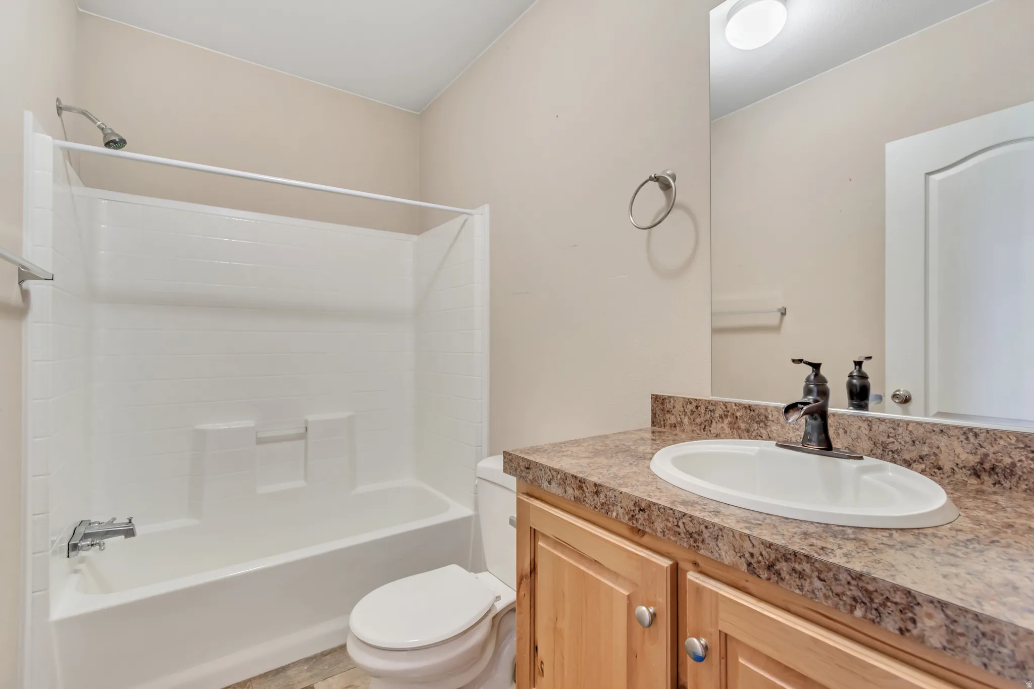 White shower-tub combination, wood-finish vanity with an integrated sink, bronze-finish faucet, mirror, and flush-mount ceiling light
