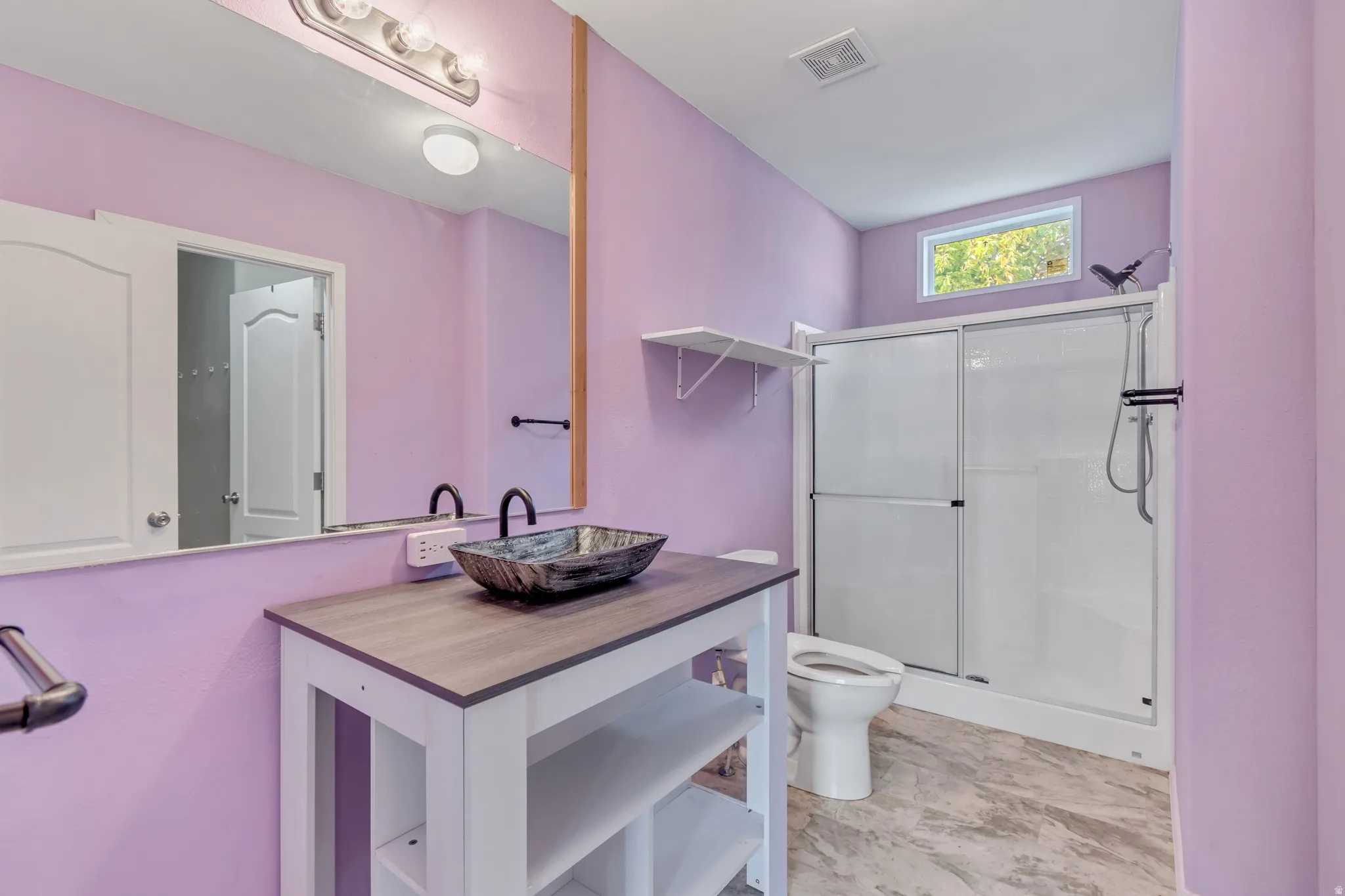 Vessel sink with a dark finish, wood-finish vanity top, wall-mounted mirror with overhead lighting, built-in shower with sliding glass doors, and a translucent window