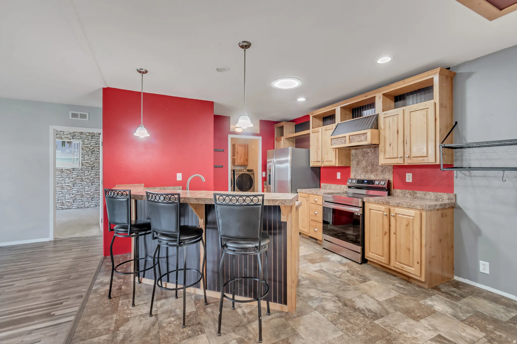 Kitchen featuring wood cabinetry, stainless steel appliances, a breakfast bar with pendant lighting, and tile-finish flooring