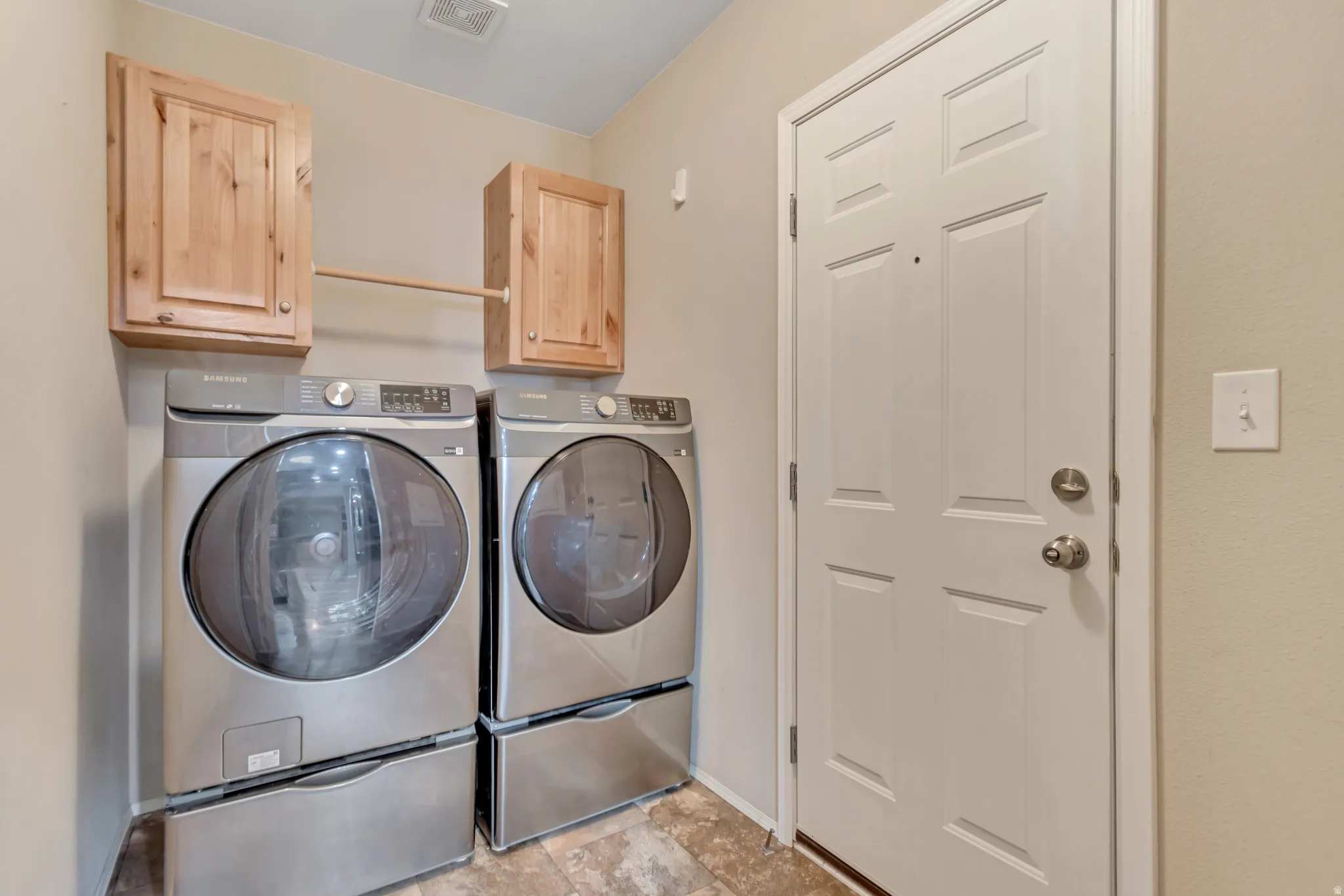 Laundry area featuring wood-finish cabinetry, a built-in hanging rod, neutral wall tones, and patterned floor tiling