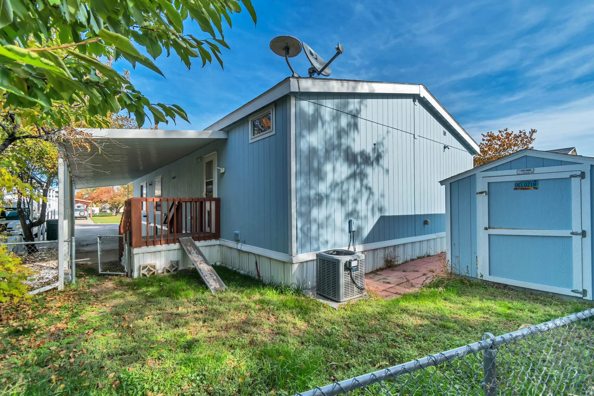 Exterior featuring light blue siding, a covered patio with wood railing, a detached storage shed, and a chain-link fence
