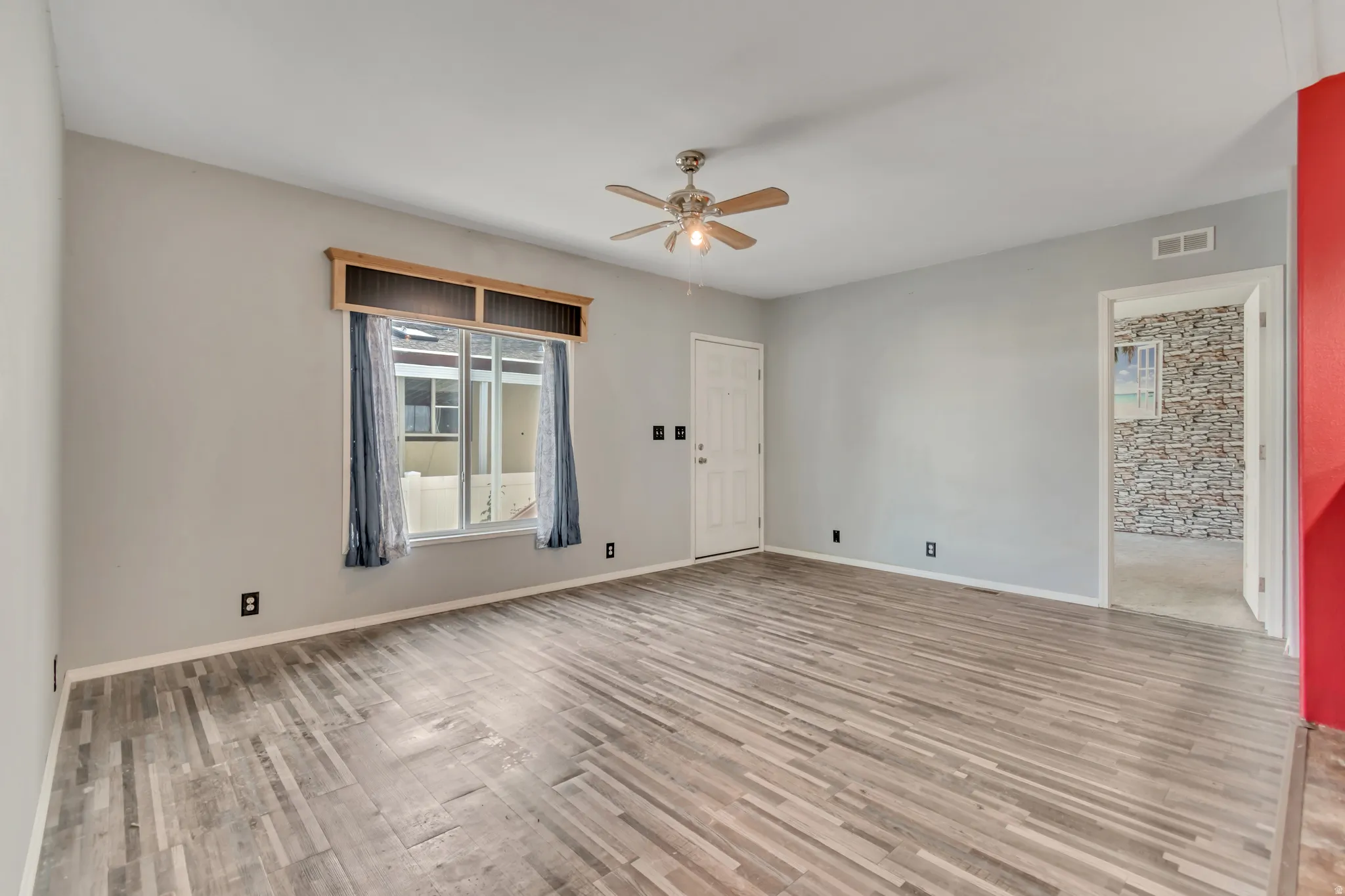 Wood-finish flooring throughout, ceiling fan with integrated lighting, and a white paneled entry door