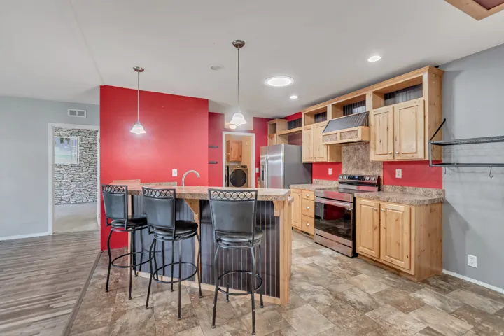 Kitchen featuring wood cabinetry, stainless steel appliances, a breakfast bar with pendant lighting, and tile-finish flooring