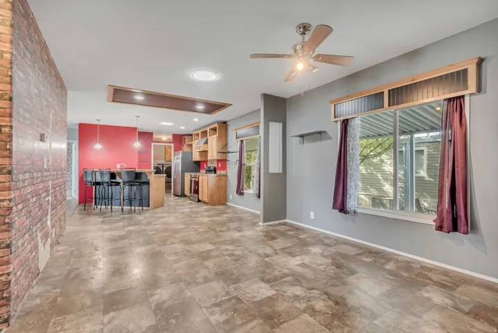 Open-concept living area with tile flooring, exposed brick wall accent, kitchen island with pendant lighting, wood cabinetry, and a ceiling fan