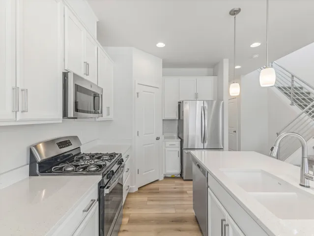 White shaker cabinetry, stainless steel appliances, light-toned countertops, wood-finish flooring, and a contemporary open-riser staircase