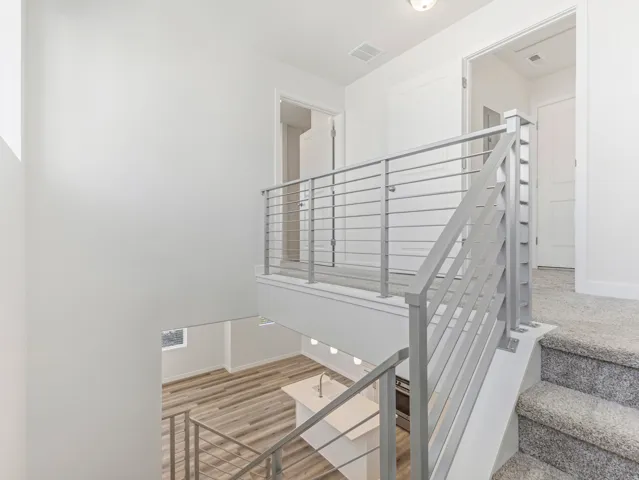 Carpeted staircase with metal railing, upper landing with carpet flooring, and lower level featuring wood-finish flooring
