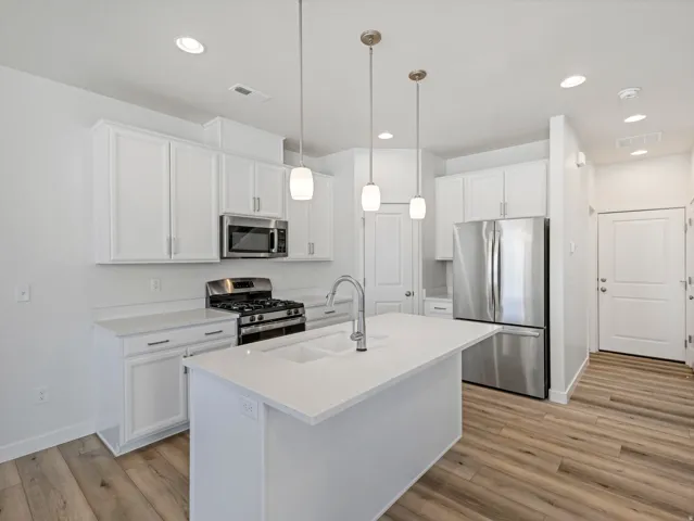 Kitchen featuring white shaker-style cabinetry, stainless steel appliances, a center island with an integrated sink, pendant lighting, and wood-finish flooring