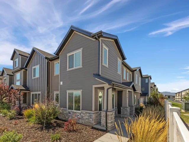 Multi-level townhome featuring horizontal and vertical siding, stone veneer accents, covered porch entrance, and mature landscaping