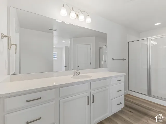 White vanity with dual sinks, a stone-finish countertop, brushed nickel hardware, and wood-finish flooring