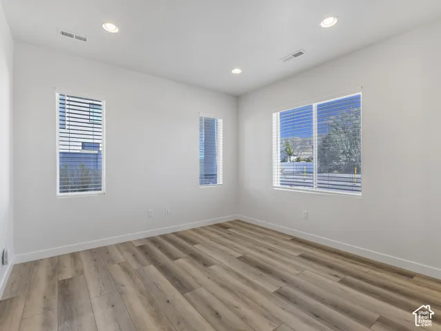Recessed ceiling lighting, multiple windows with blinds, wood-finish flooring, and white baseboards