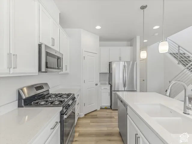 White shaker cabinetry, stainless steel appliances, light-toned countertops, wood-finish flooring, and a contemporary open-riser staircase