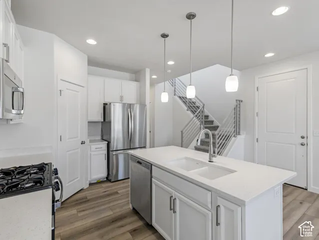 Kitchen featuring a central island with an undermount sink, stainless steel appliances, white cabinetry, wood-finish flooring, and recessed lighting