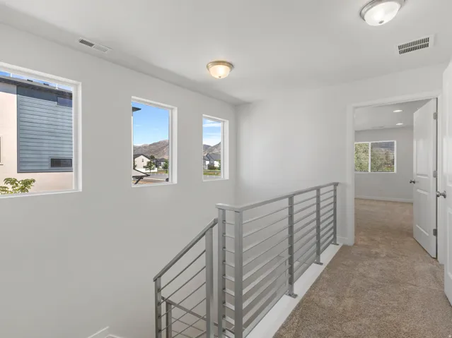 Upper-level landing featuring a contemporary metal railing, plush carpeting, and three windows showcasing mountain scenery