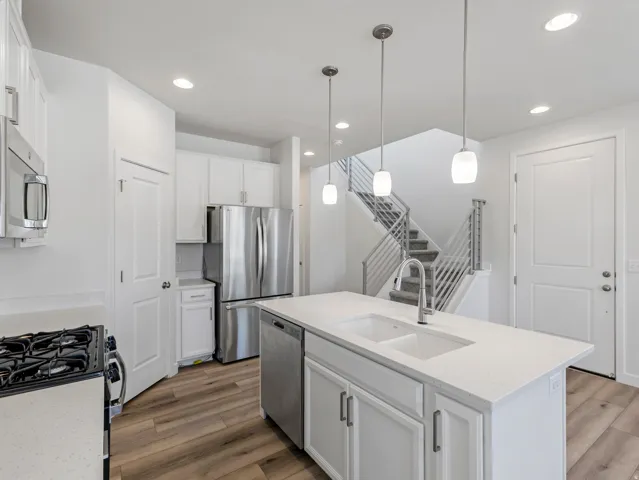 Kitchen featuring a central island with an undermount sink, stainless steel appliances, white cabinetry, wood-finish flooring, and recessed lighting