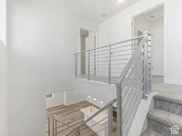 Carpeted staircase with metal railing, upper landing with carpet flooring, and lower level featuring wood-finish flooring