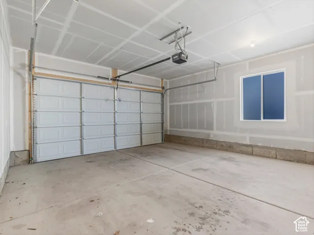 Concrete flooring, white paneled garage door, automatic garage door opener, interior window, overhead lighting