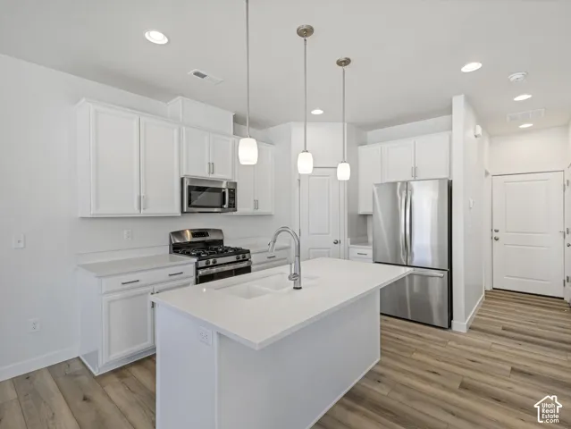 Kitchen featuring white shaker-style cabinetry, stainless steel appliances, a center island with an integrated sink, pendant lighting, and wood-finish flooring
